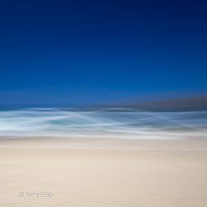 Bewußte Kamerabewegung (ICM)ICM Beach Art mit Wellenlinien aus den Schaumkronen der Wellen und beigem Sandstrand und tiefblauem Himmel, kreativ verwischt durch ziehen der Kamera während der Aufnahme