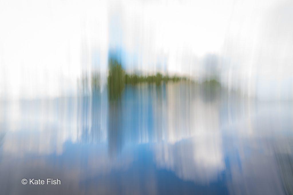 Bewusste Kamerabewegung ICM einer grünen Insel in einem See mit Spiegelung bei vertikaler Bewegung der Kamera