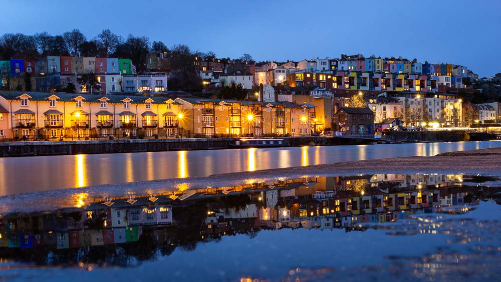 Blaue Stunde in Bristol am Hafen mit den bunten Häusern von Hotwells und den Lichtern, die sich im Wasser spiegeln. Langzeitbelichtung