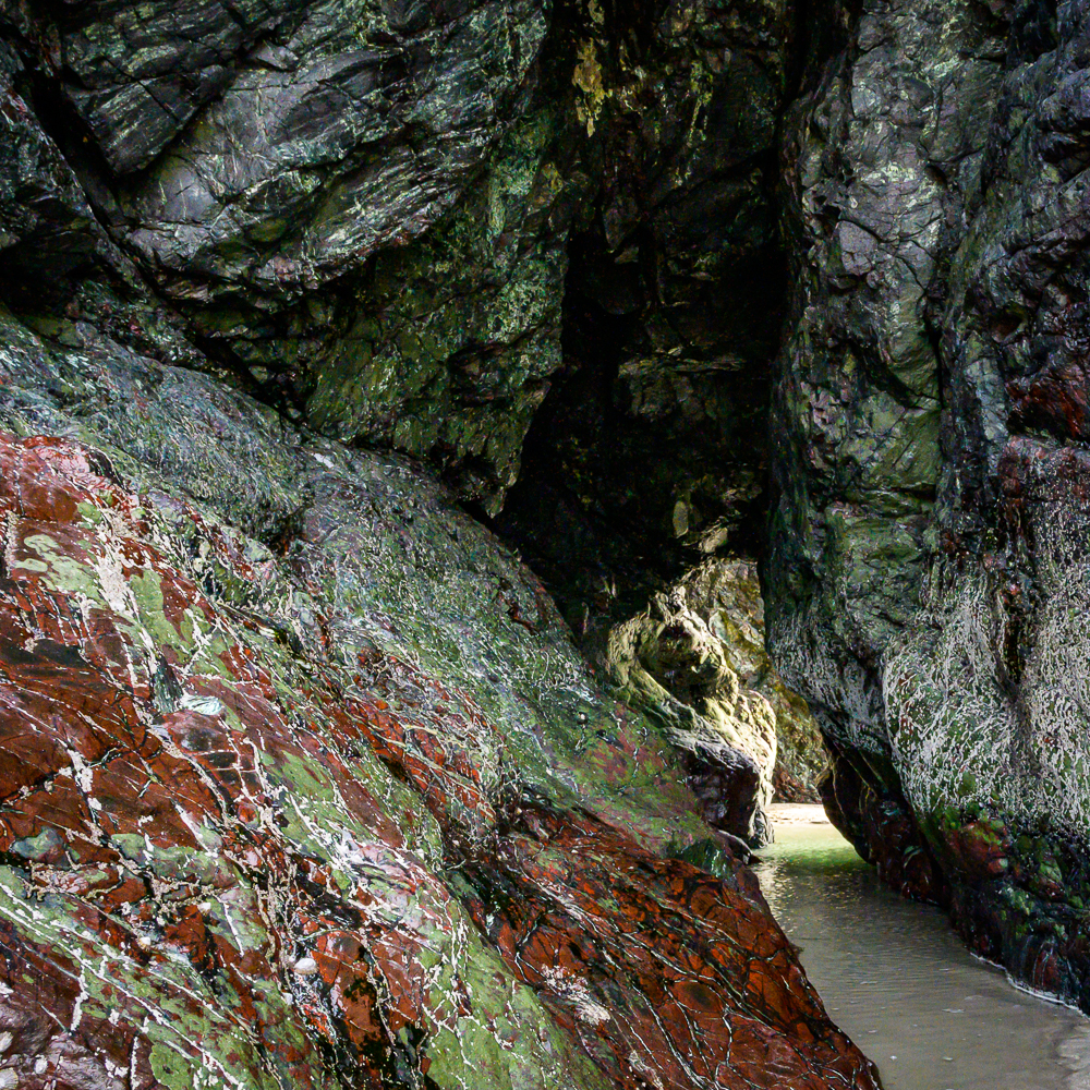 Kynance Cove at the Lizard Cornwall Serpentinin, Höhlenartiger Felsendurchgang, mit toller rot und grüner Färbung des hier typischen Serpentinit Gesteins in der Kynance Cove auf der Lizard Halbinsel in Cornwall