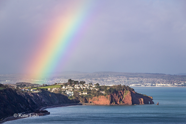 Regenbogen fotografieren mit Telebrennweite und Fokus auf die Landschaft am Ende des Regenbogens
