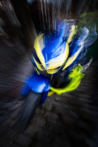 Bewusst bewegte Kamera in form von zoom burst ICM eines blau gelben Motorrads, das dadurch erscheint als würde es fliegen.