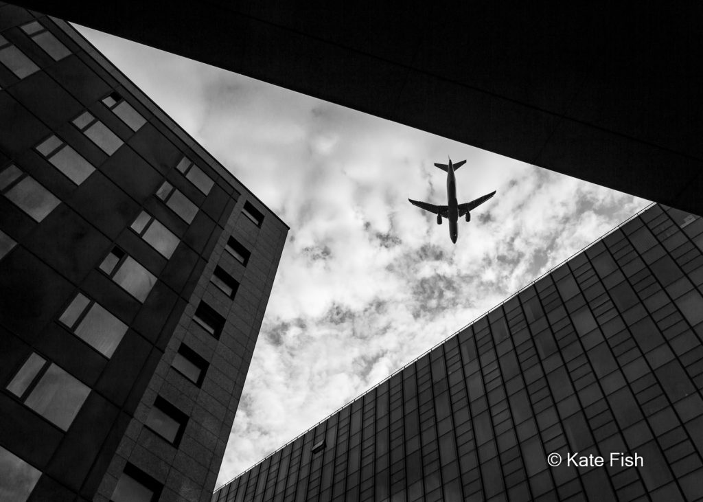 Schwarzweißfotografie Flugzeugsilhouette über Hochhäusern als Motivbeispiel