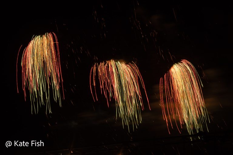 3 jeweils 3 farbige Leuchtbüschel (rot, gelb, grün) während einer Feuerwerksshow fotografiert.